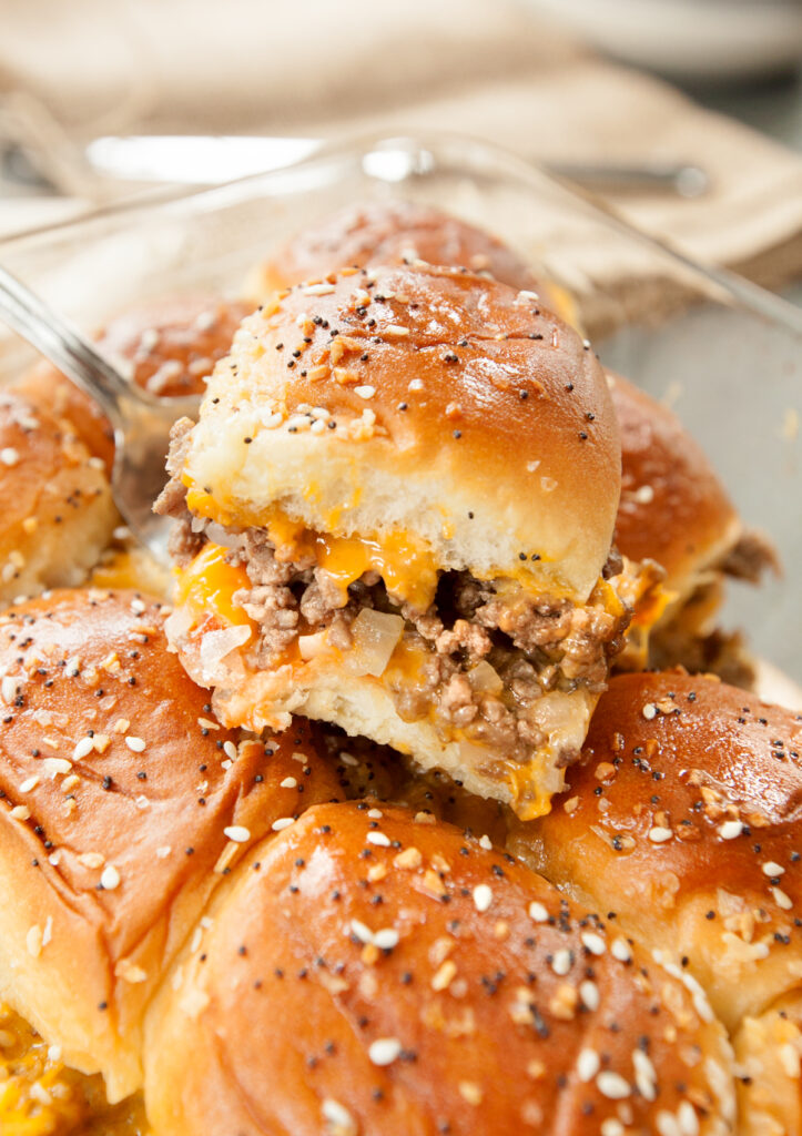 A spatula scooping out a cheeseburger slider using soft sweet Hawaiian rolls.