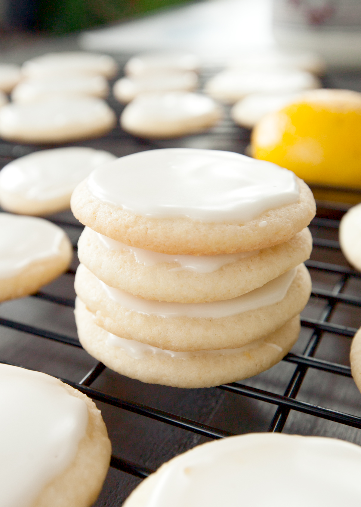 A stack of iced lemon cookies on a cookie rack with a lemon in the background.