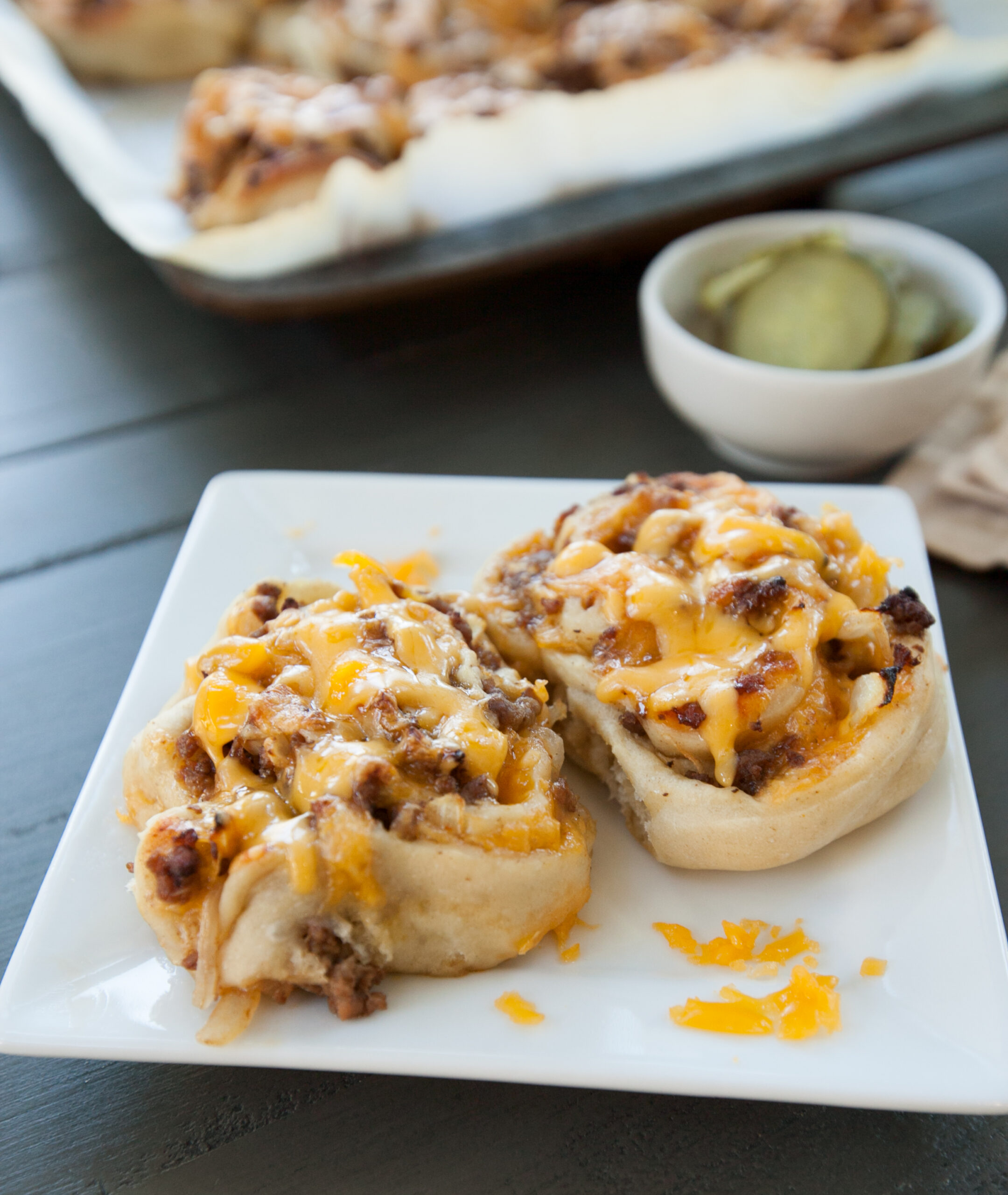 A plate of cheeseburger pinwheels covered in ooey gooey cheese.