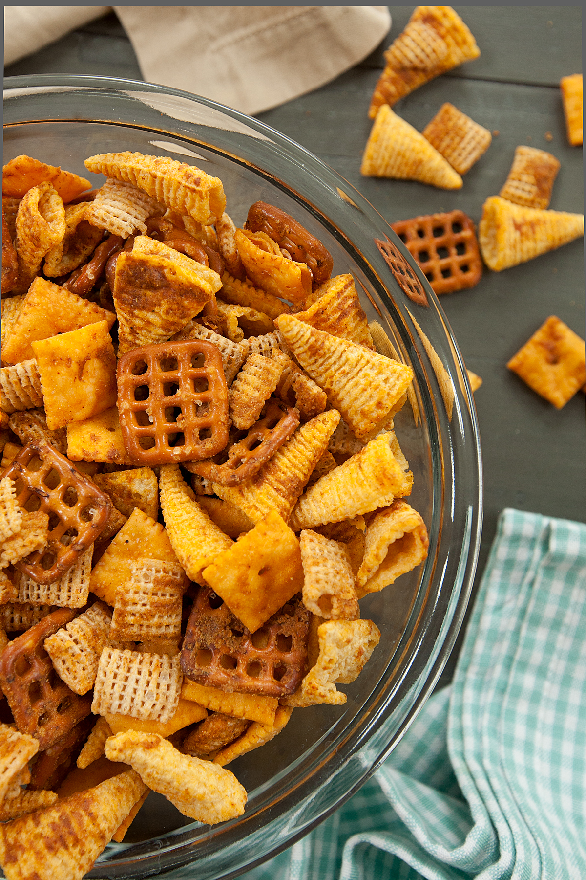 Close up view of homemade cheese chex mix in a glass bowl with a blue and white gingham napkin nearby.