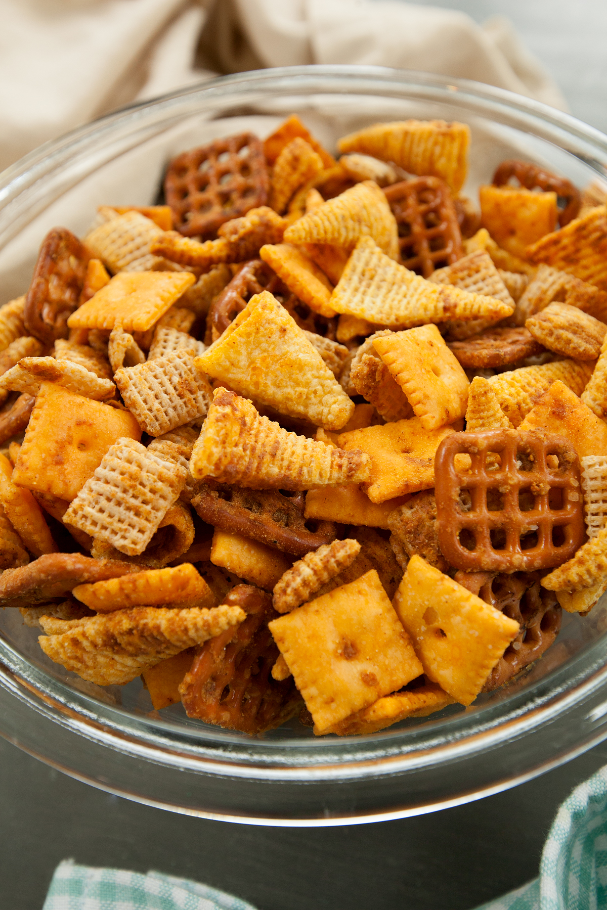 Homemade chex mix with visible bright orange cheesy flavors, packed into a glass bowl.