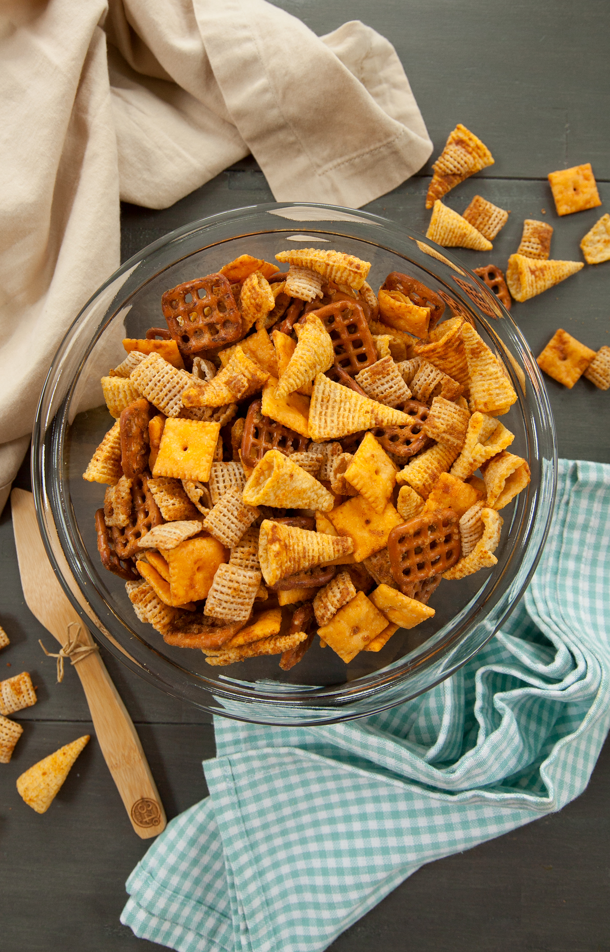 Overhead view of a glass bowl of cheese chex mix with a few pieces scattered on the table.