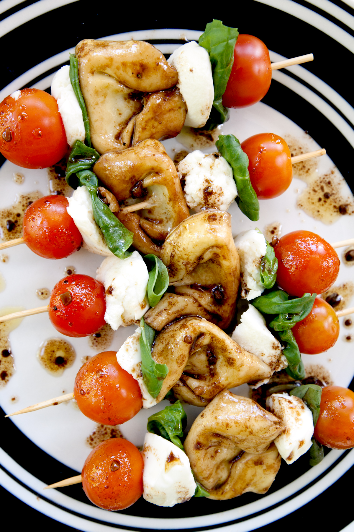 Overhead view of caprese skewers with marinated tortellini lined up on a plate and covered with balsamic vinaigrette. 