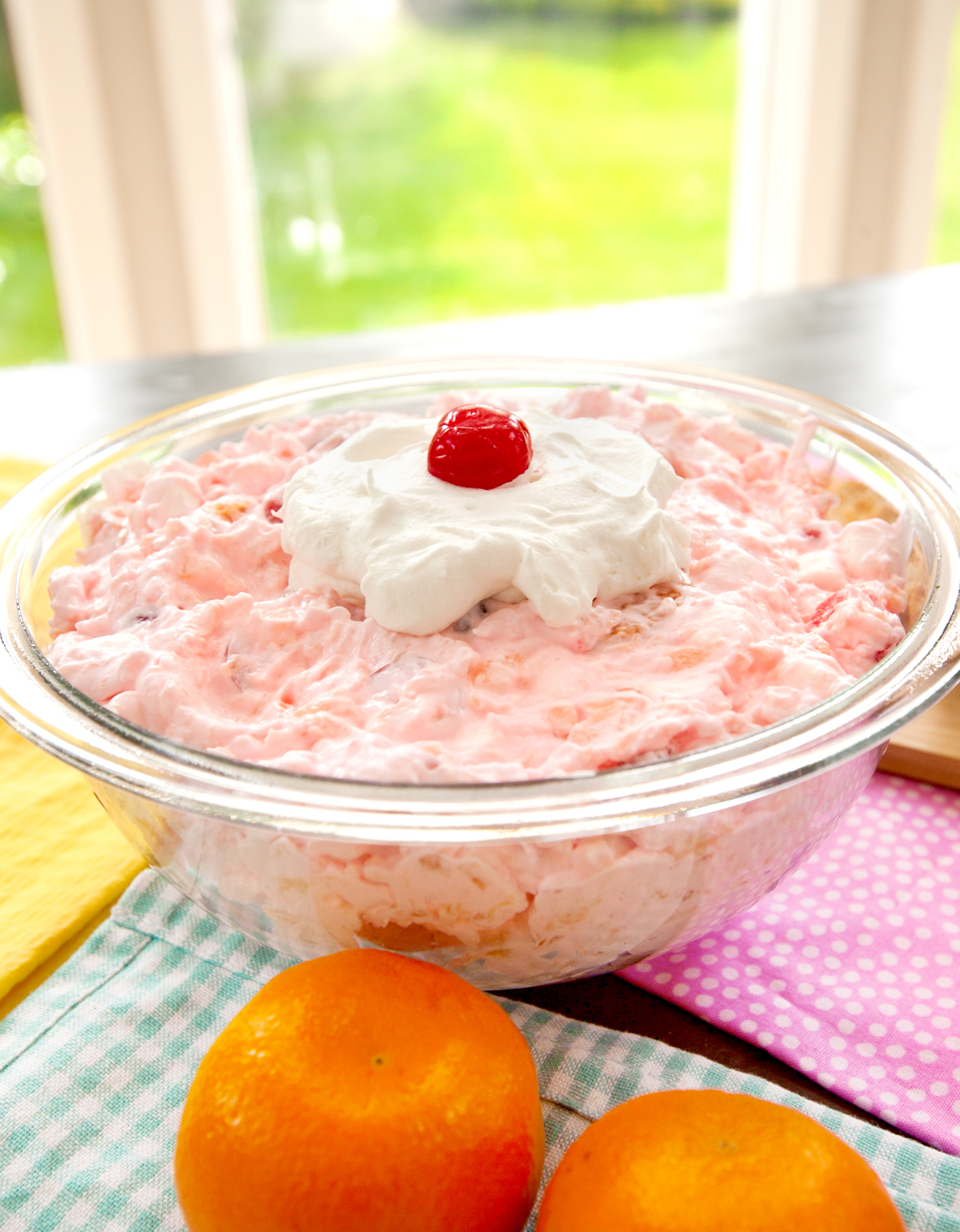 A colorful serving bowl of ambrosia salad sits near a sunny window.