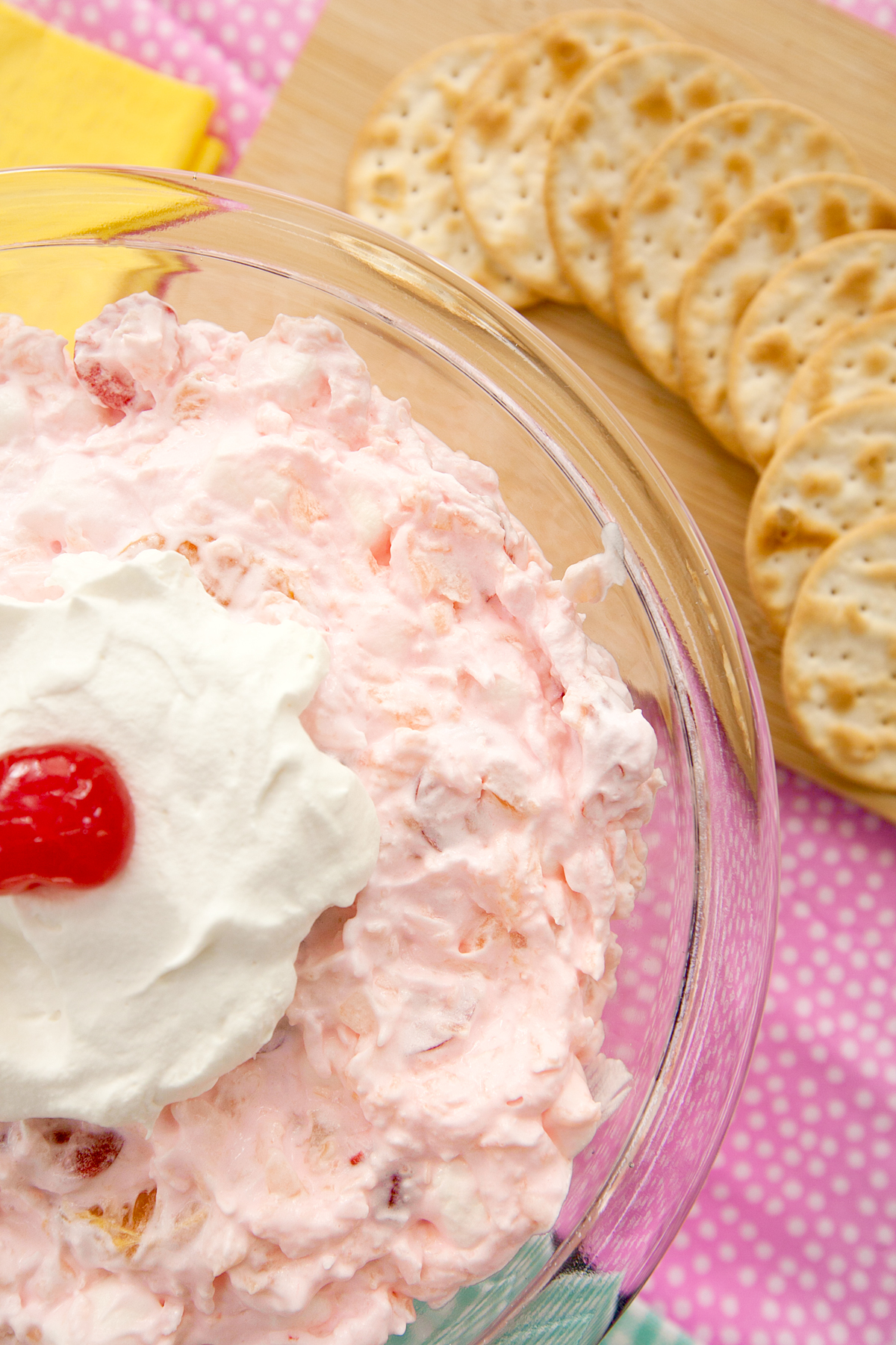 A close up view of pink fluffy ambrosia salad garnished with a cherry.