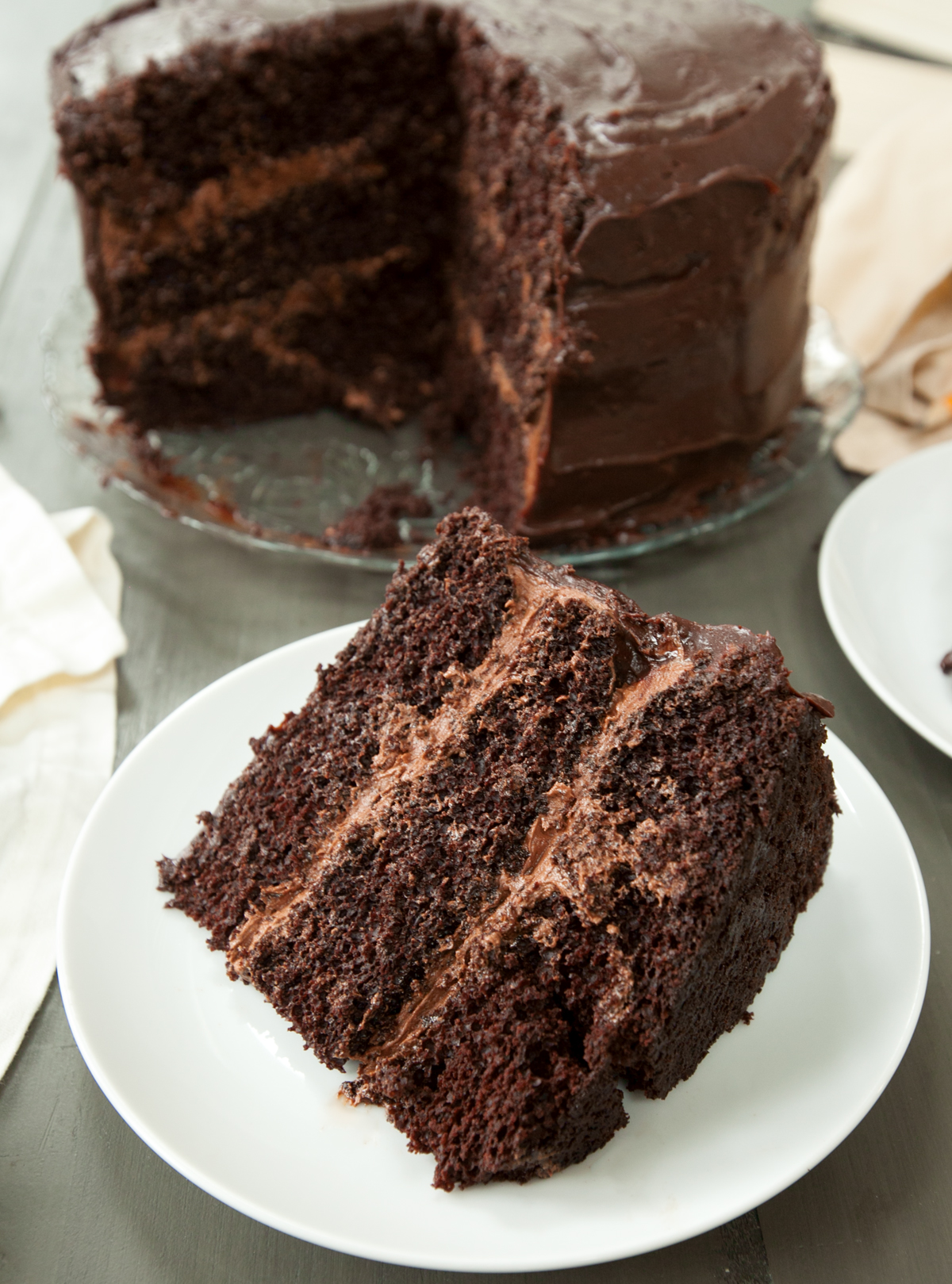 A fudgy triple layer Matilda chocolate cake with a thick slice taken out and placed on a plate.