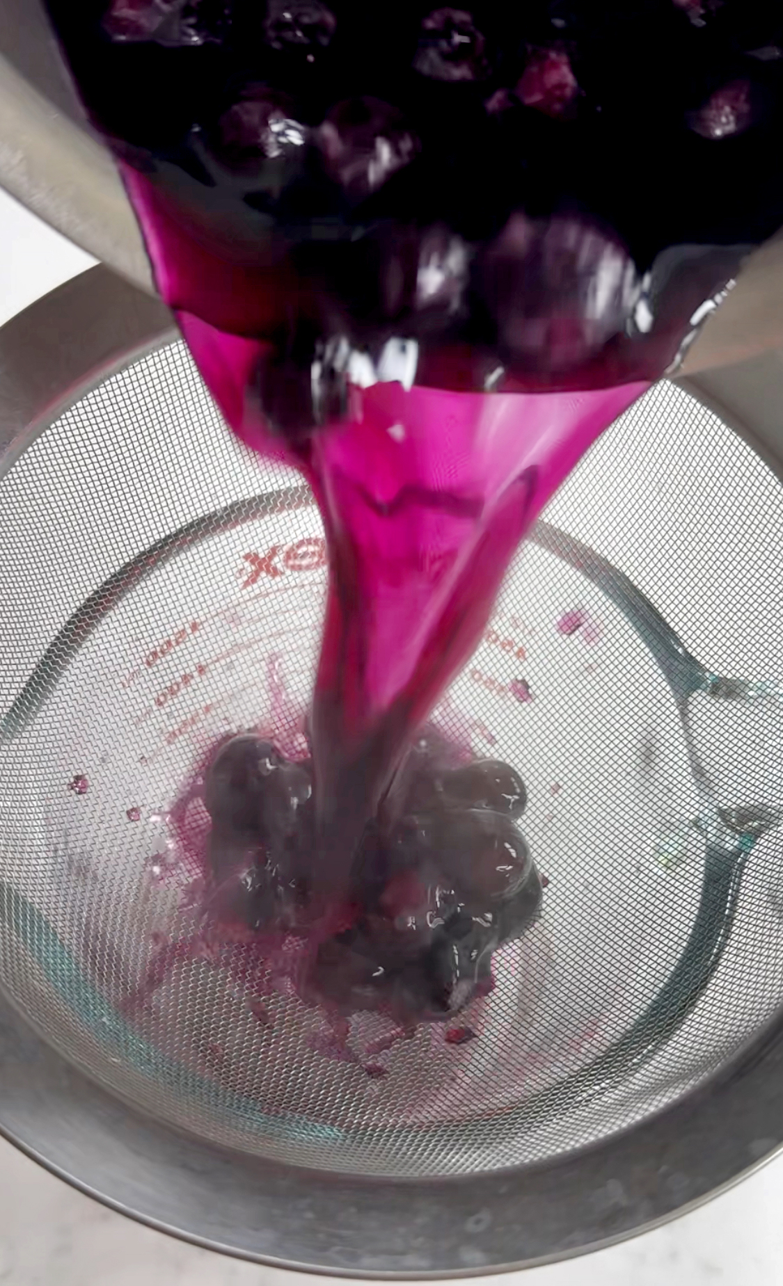cooked blueberry syrup being poured through a strainer.