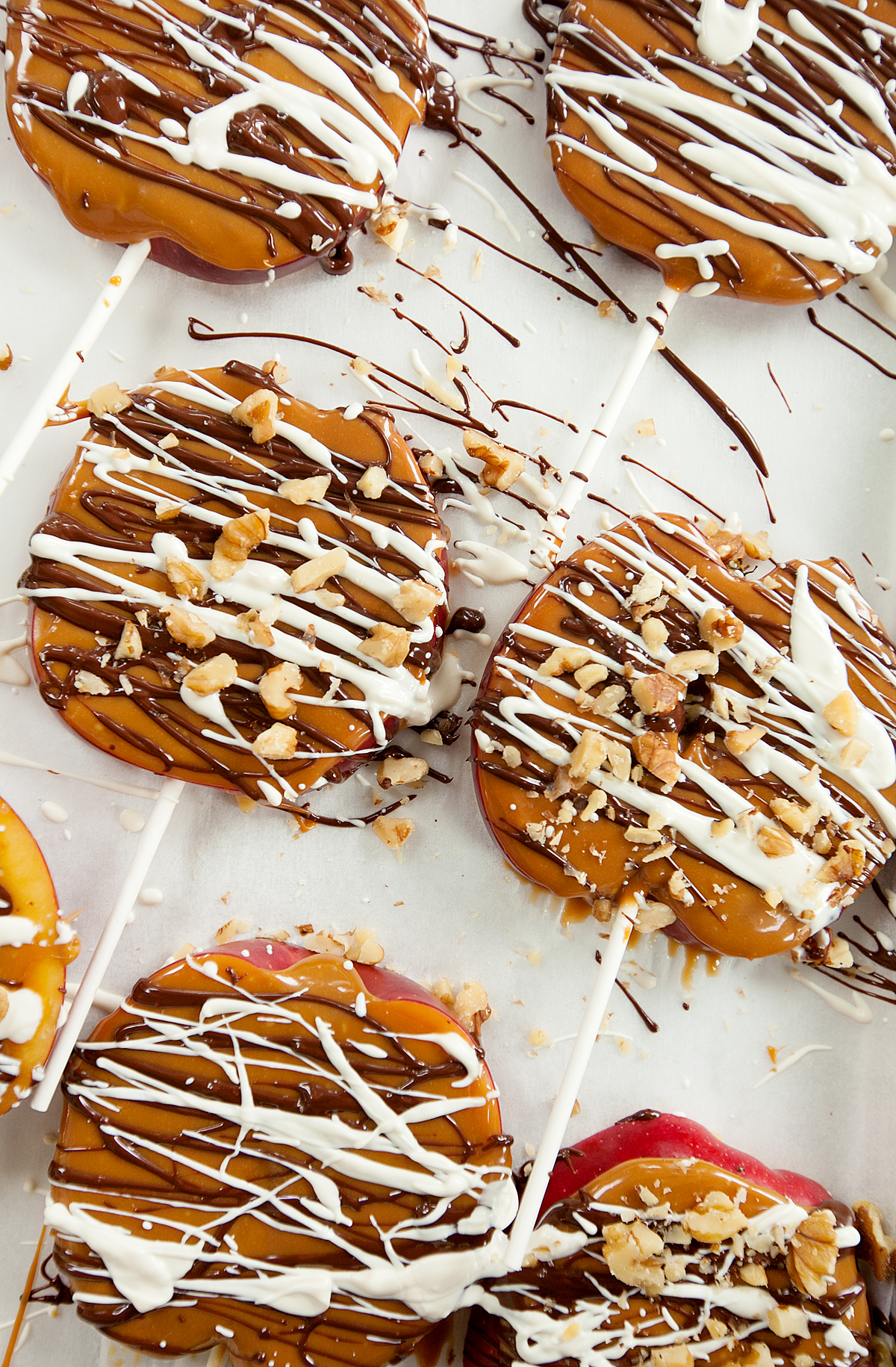 Overhead view of a pan of caramel apple slices drizzled with white and dark chocolate and chopped nuts.